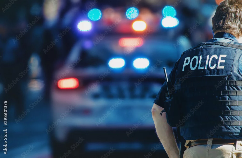  Polizeibeamter mit Schutzweste vor Polizeifahrzeugen mit eingeschaltetem Blaulicht