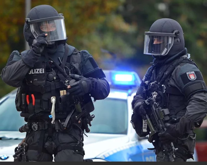  Zwei Polizeibeamte in taktischer Schutzausrüstung vor einem Polizeifahrzeug mit Blaulicht