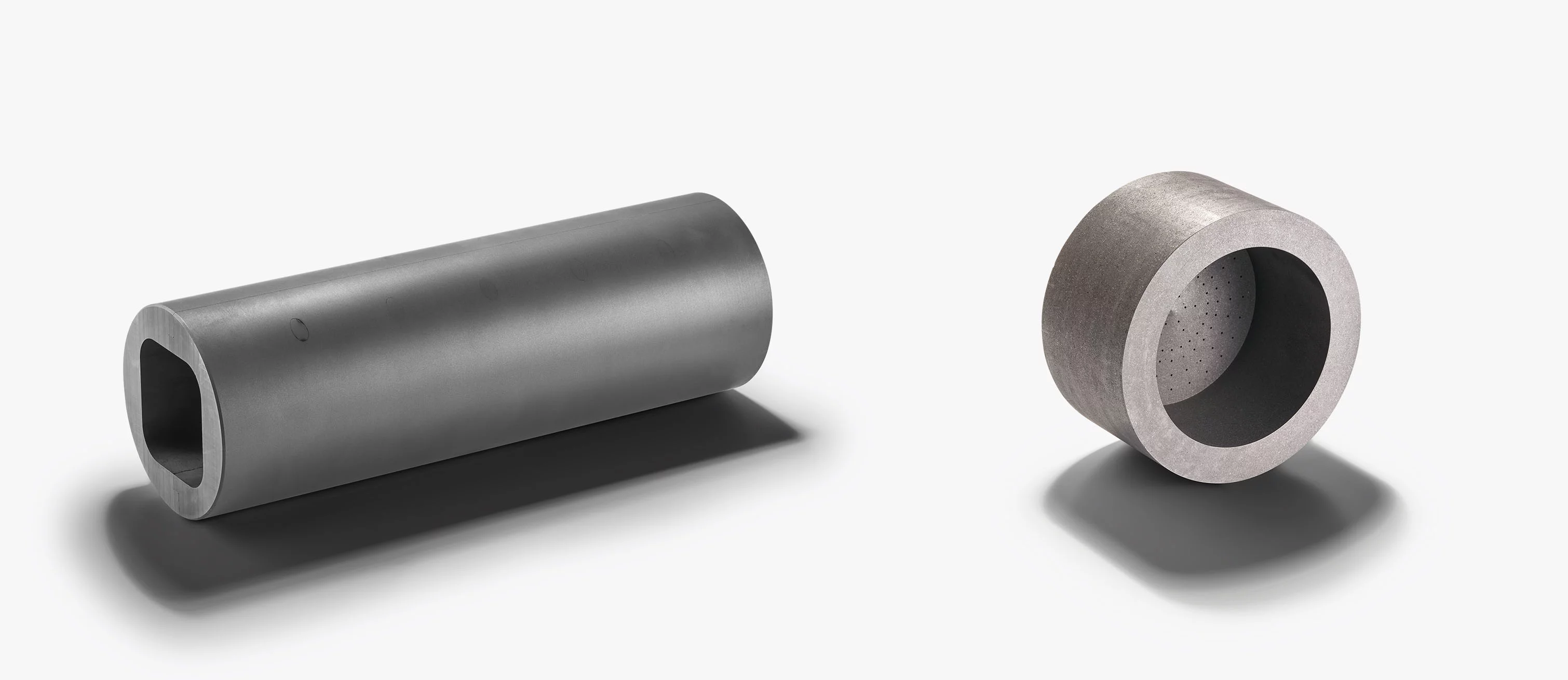 Zwei unterschiedliche hohle Zylinderbauteile aus einem technischen Werkstoff, vermutlich Graphit, auf hellem Hintergrund.