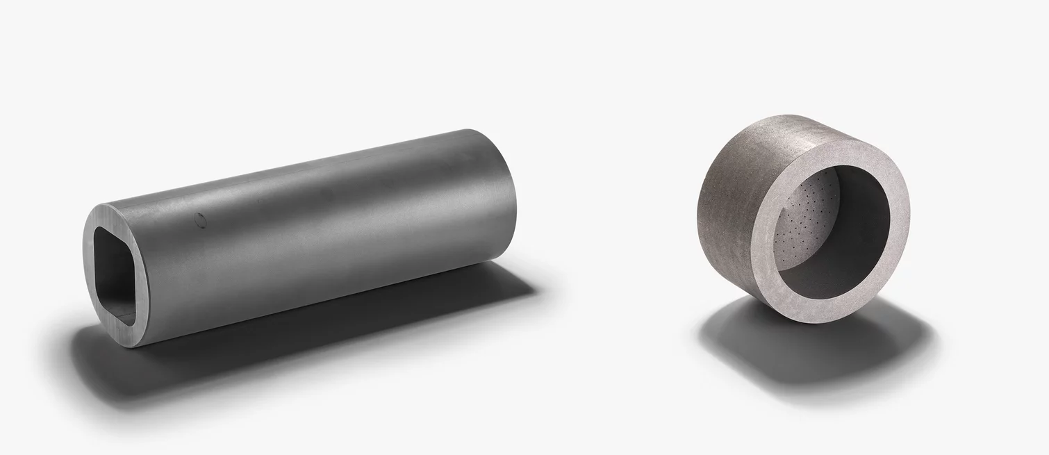  Zwei unterschiedliche hohle Zylinderbauteile aus einem technischen Werkstoff, vermutlich Graphit, auf hellem Hintergrund.