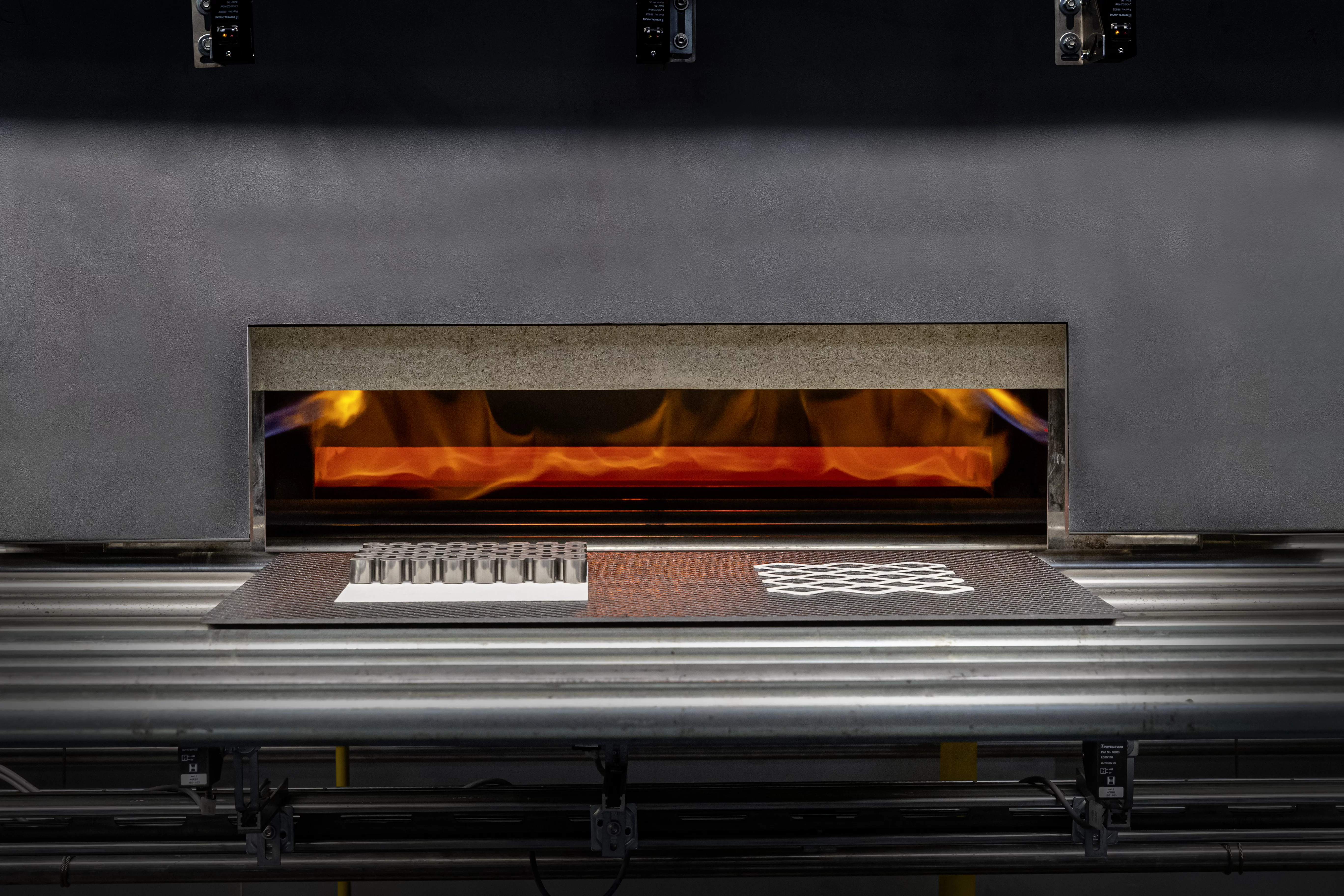  Industrieller Ofen mit sichtbarer Flamme zur thermischen Behandlung von Bauteilen aus technischer Keramik oder Metall auf einem Fördersystem.