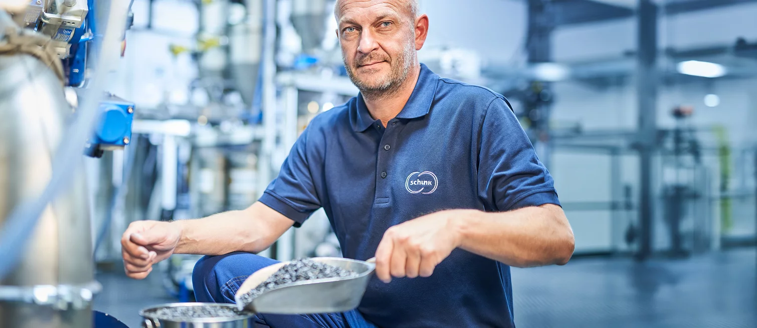  A Schunk Group employee holds a scoop of granular raw material in a production environment.