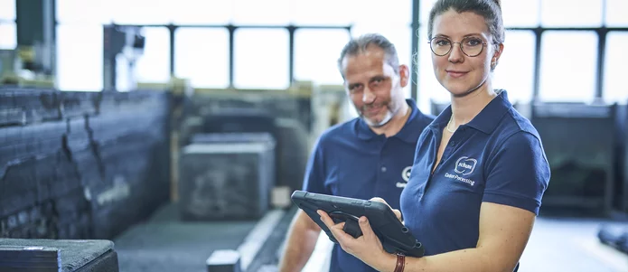  Zwei Mitarbeitende der Schunk Group in der Produktion, eine Frau hält ein Tablet zur digitalen Kontrolle von Fertigungsprozessen.