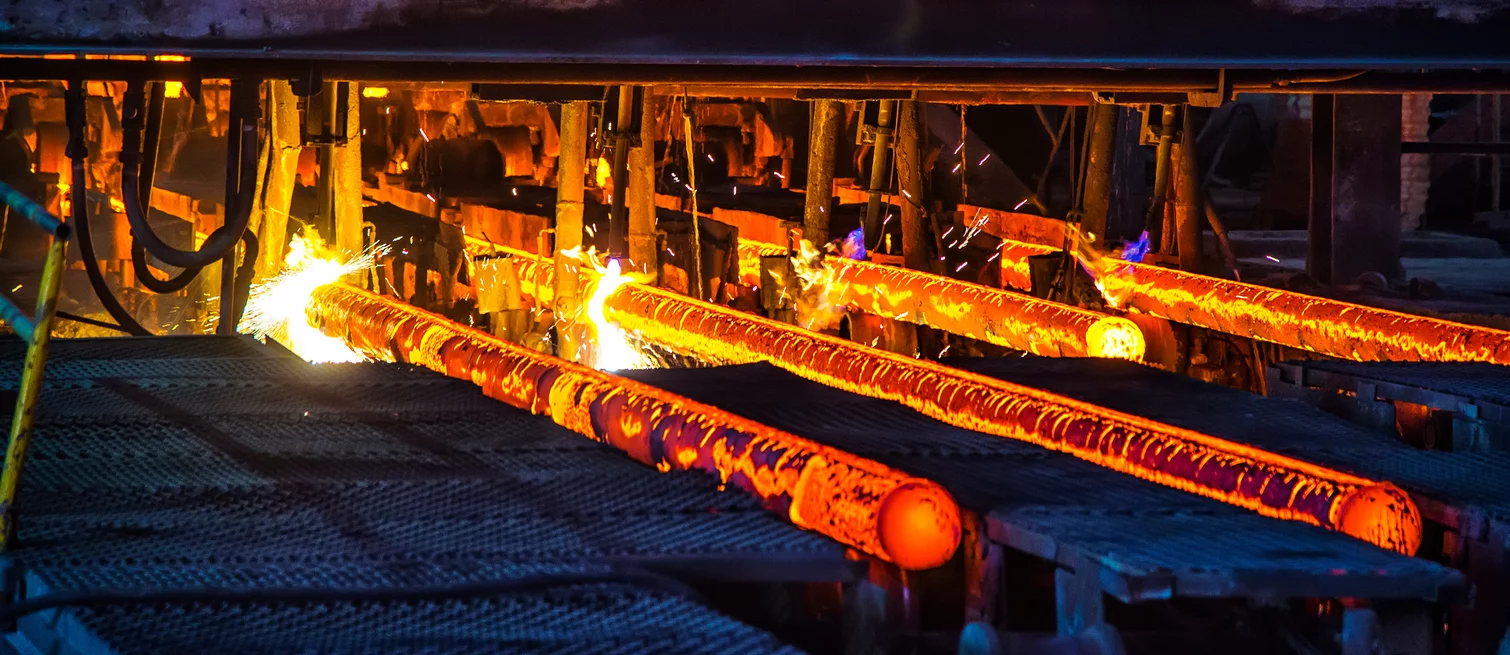  Glühende Metallstäbe beim Stranggießen in einer Stahlwerkanlage, umgeben von Funken und Hitze.