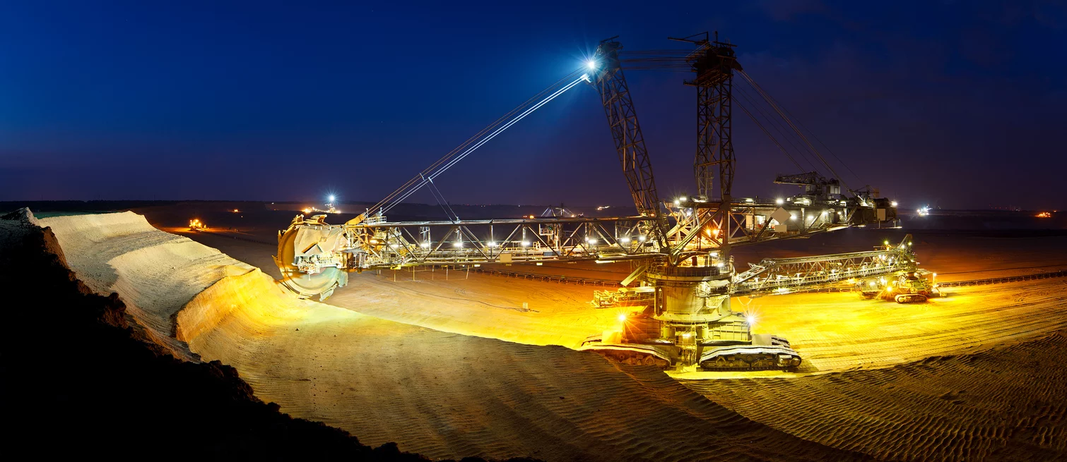  A brightly illuminated bucket-wheel excavator in night-time operation at an open-pit mine for raw material extraction.