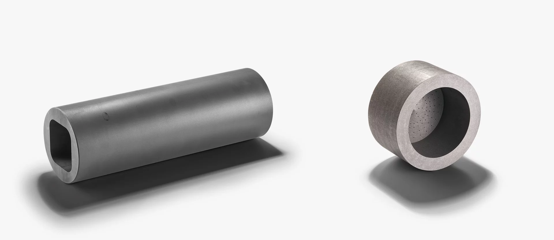  Two different hollow cylindrical components made of a technical material, likely graphite, placed on a light background.