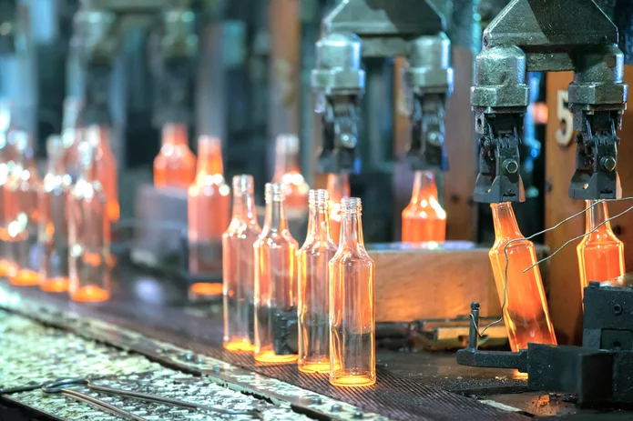  Glass bottles in production: glowing hot bottles on a conveyor belt beneath automated forming tools in a glass factory.