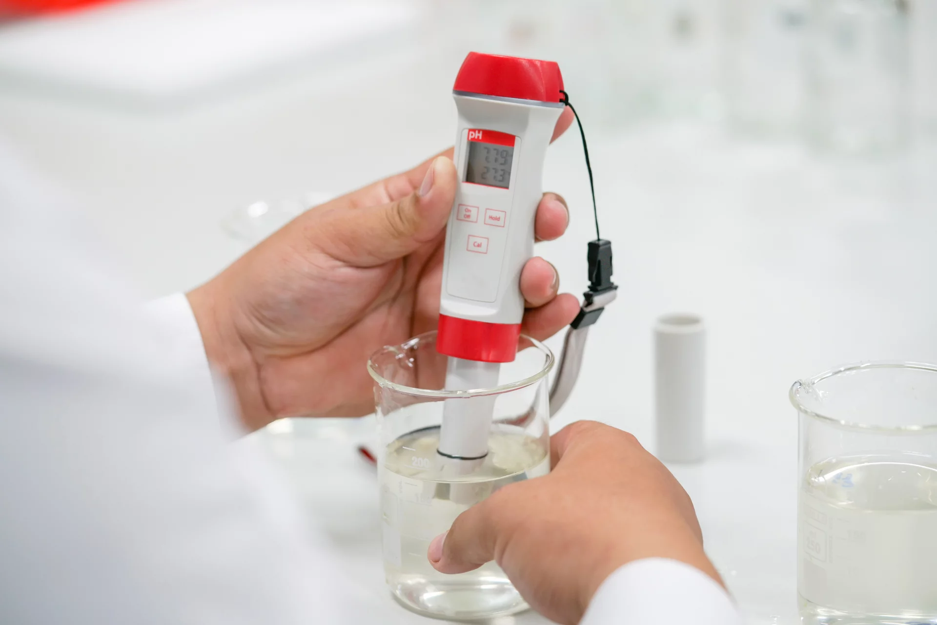  Laboratory scene at Schunk: A hand holds a digital pH meter in a beaker containing liquid for quality control.