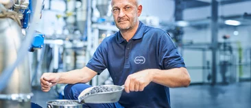  Ein Mitarbeiter der Schunk Group hält eine Schaufel mit körnigem Werkstoffgranulat in einer Produktionsumgebung.