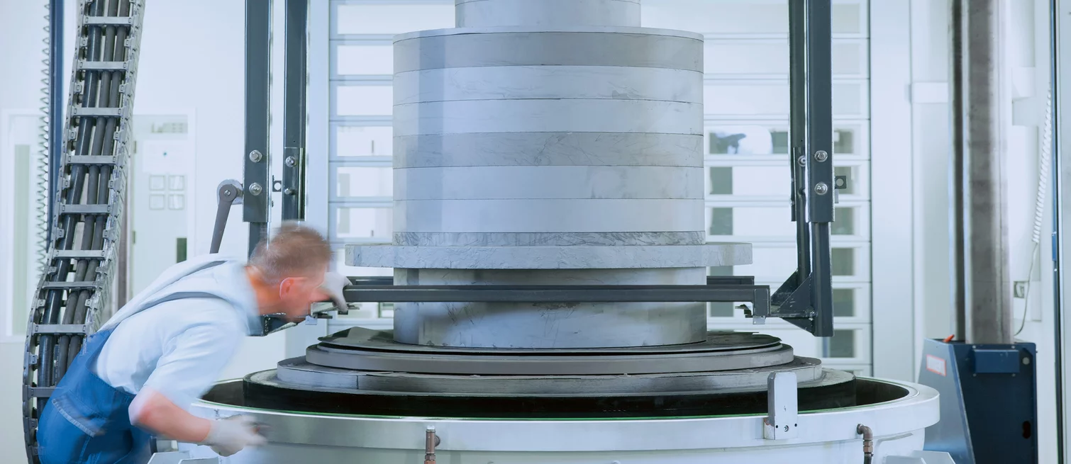 Mitarbeiter in der Fertigung kontrolliert ein großes zylindrisches Bauteil aus Graphit oder technischer Keramik auf einer Industriemaschine.