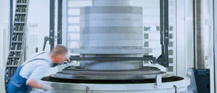  Mitarbeiter in der Fertigung kontrolliert ein großes zylindrisches Bauteil aus Graphit oder technischer Keramik auf einer Industriemaschine.