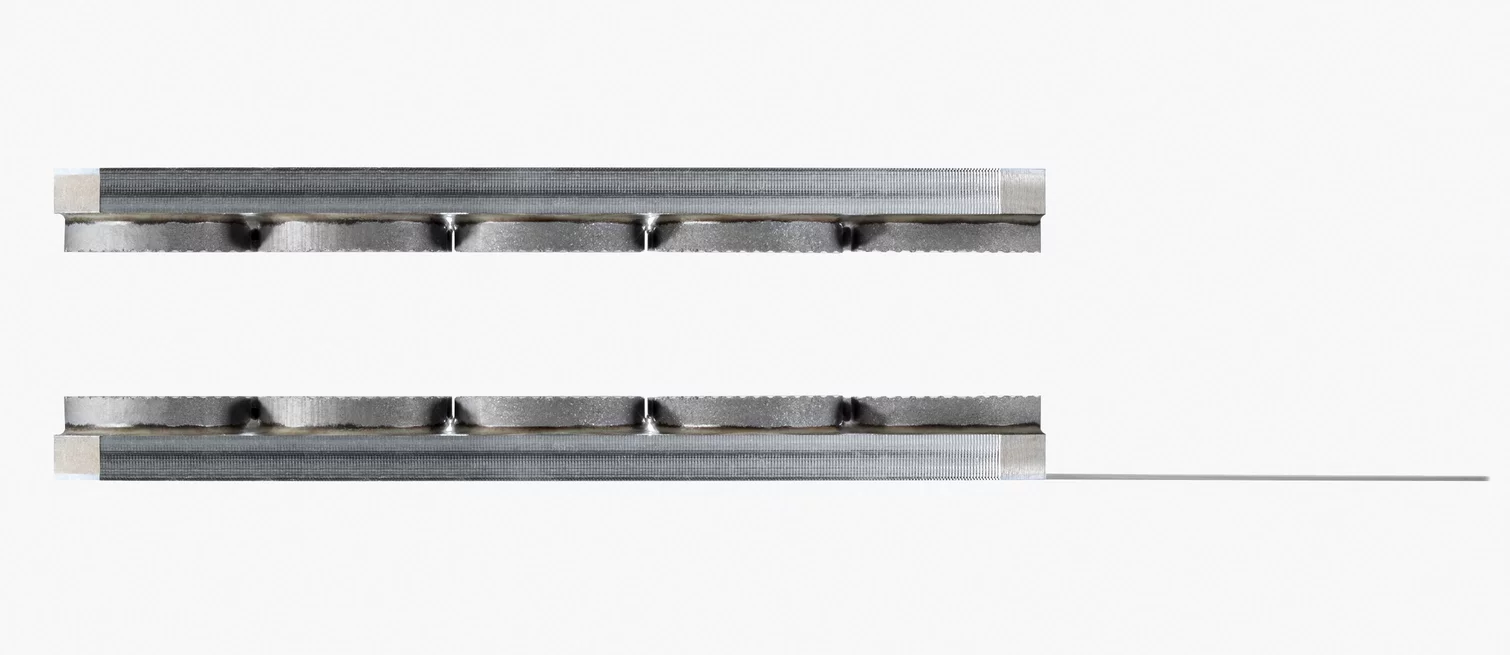  Two metallic precision components with a grooved surface for guiding a thin strip or wire material.