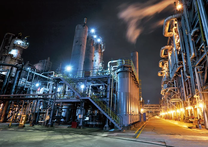  Beleuchtete Industrieanlage mit Rohrleitungen, Türmen und Dampfaustritt bei Nacht – vermutlich aus der Chemie-, Petrochemie- oder Energiebranche.
