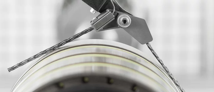 Close-up of a mounted electrical sliding contact with carbon brush and braided wire connection on a rotating slip ring.