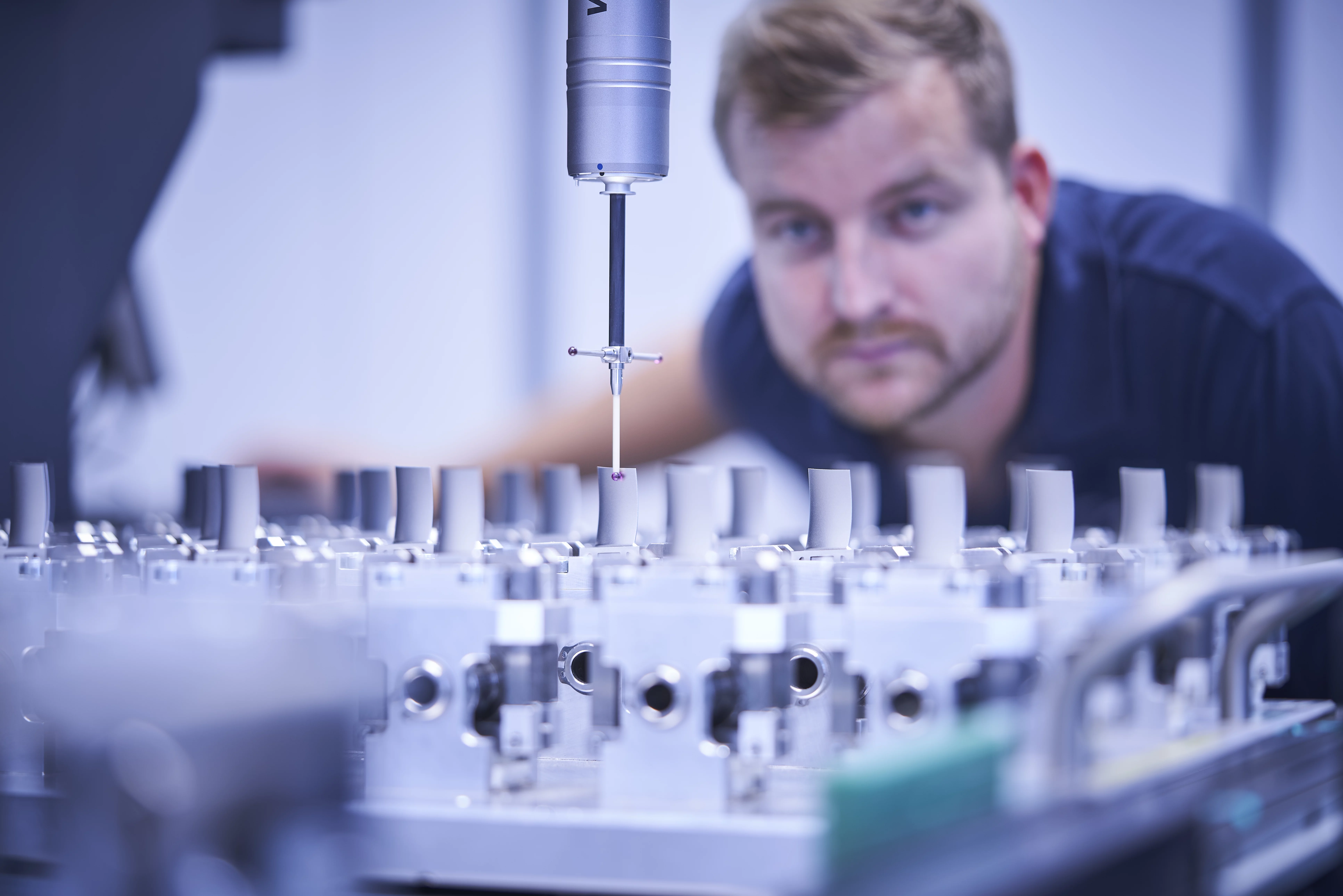  Mitarbeiter überwacht eine präzise Messung an Bauteilen mit einer Koordinatenmessmaschine in einer technischen Umgebung.