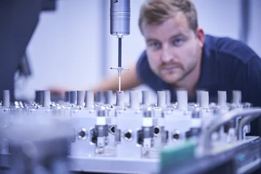  Mitarbeiter überwacht eine präzise Messung an Bauteilen mit einer Koordinatenmessmaschine in einer technischen Umgebung.