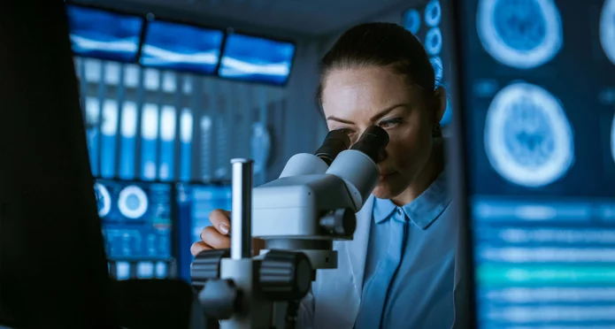  Scientist examines a sample under a microscope in a laboratory, surrounded by screens with medical scans and data.