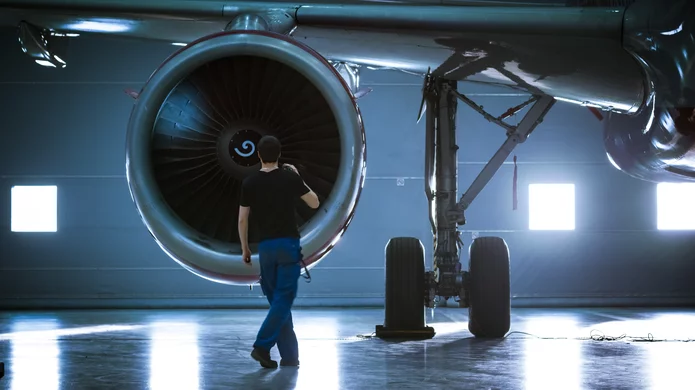Technician inspects an aircraft engine in a brightly lit maintenance hangar
