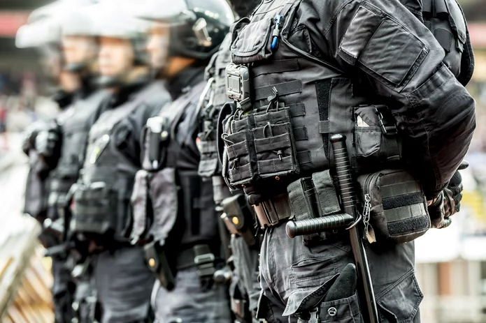  A line of police officers in tactical gear and body armour stand in formation, ready for action, focusing on equipment and uniforms.