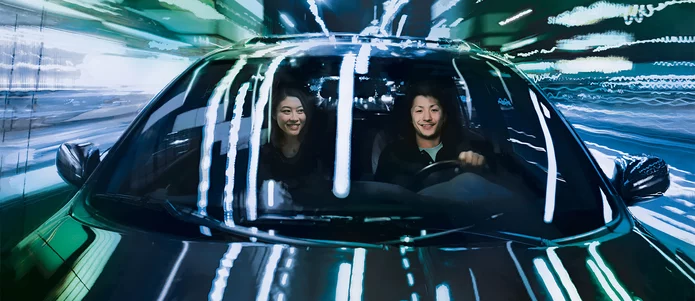  Two people drive electric car in darkness through illuminated city