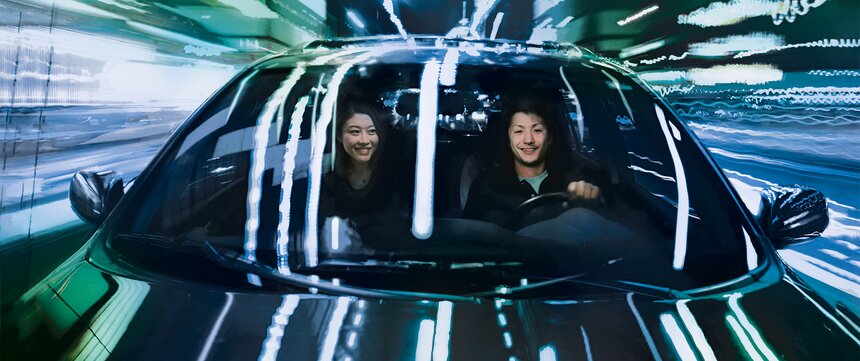  Two people drive electric car in darkness through illuminated city