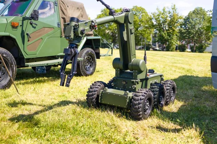  Mobiler unbemannter Roboter mit Manipulatorarm neben einem gepanzerten Einsatzfahrzeug