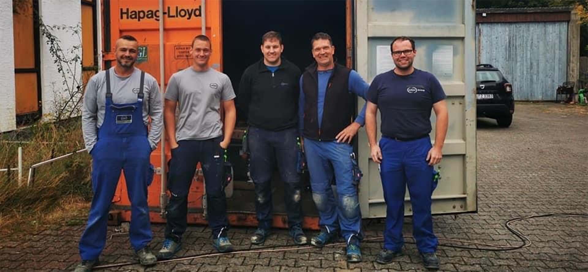  Five members of the Schunk team of helpers in the Ahr Valley are standing in front of a container.
