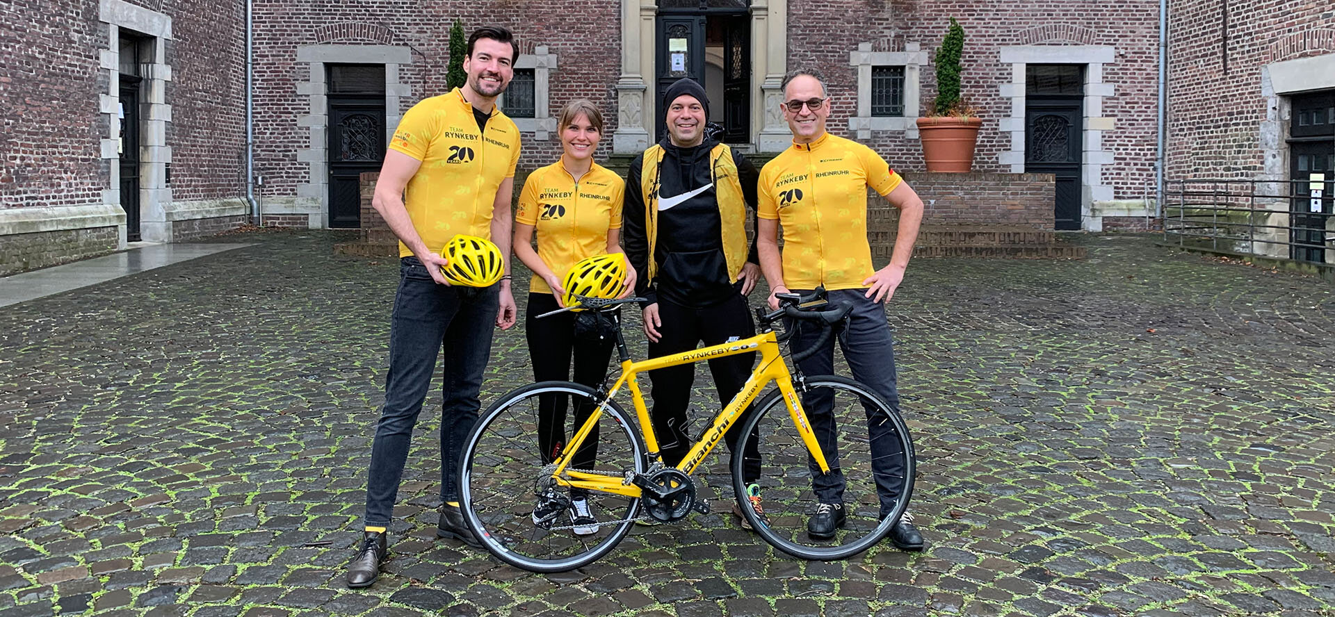  4 members of Team Rynkeby in team clothing with a yellow bicycle