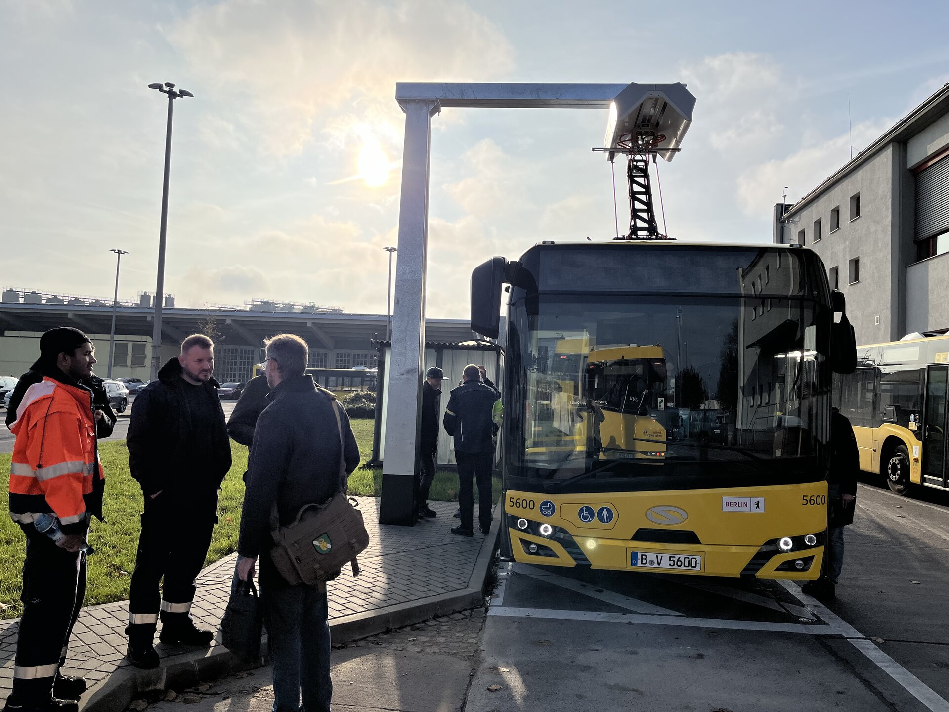 An electric bus being charged under a Schunk pantograph at a fast-charging station, with several people in work attire nearby.