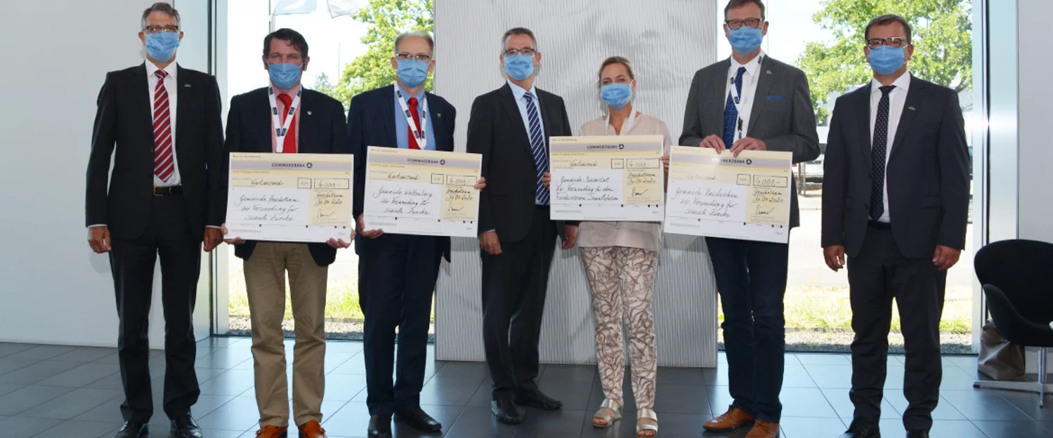 7 people stand next to each other in a row and hold the donation cheque