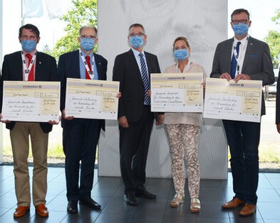 7 Personen stehen nebeneinander in einer Reihe und halten den Spendencheck