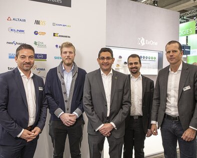 5 Mitarbeiter von Schunk und ExOne stehen vor einem Messestand