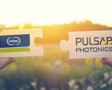 Zwei Puzzleteile mit dem Logo von Schunk und Pulsar werden von zwei Händen nebeneinander gehalten