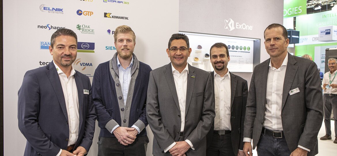 5 Schunk and ExOne employees stand in front of a trade fair stand