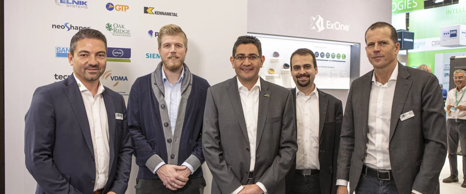 5 Schunk and ExOne employees stand in front of a trade fair stand