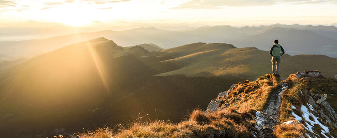Ein Mann steht auf einem Berg und betrachtet das vor ihm liegende Alpen Panorama