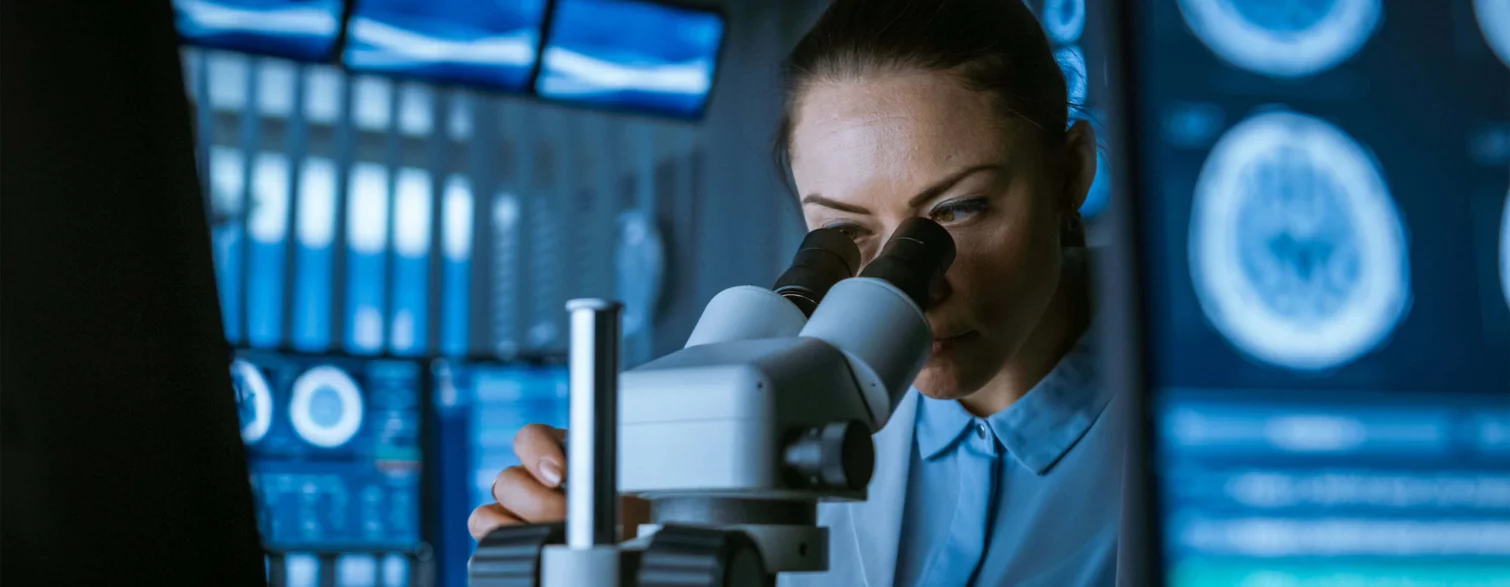  Doctor looks through a microscope and examines something, in the background there are images of a computer tomography