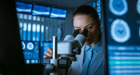  Doctor looks through a microscope and examines something, in the background there are images of a computer tomography