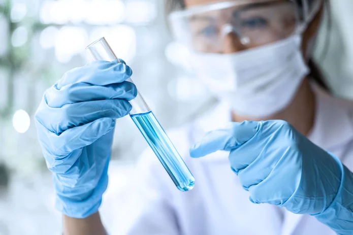  Pharmacist in protective goggles and mask examining liquid in a test tube