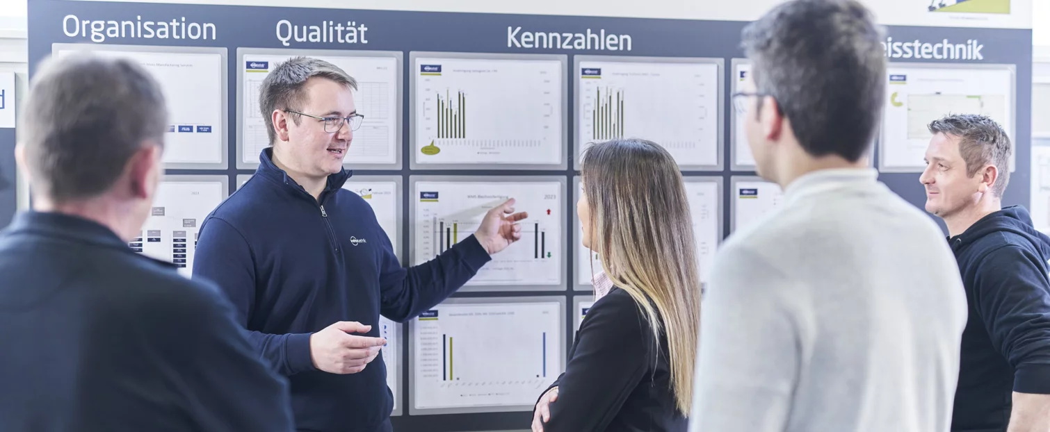  Schunk Group employees at a meeting on key figures in front of a whiteboard with various graphics and information