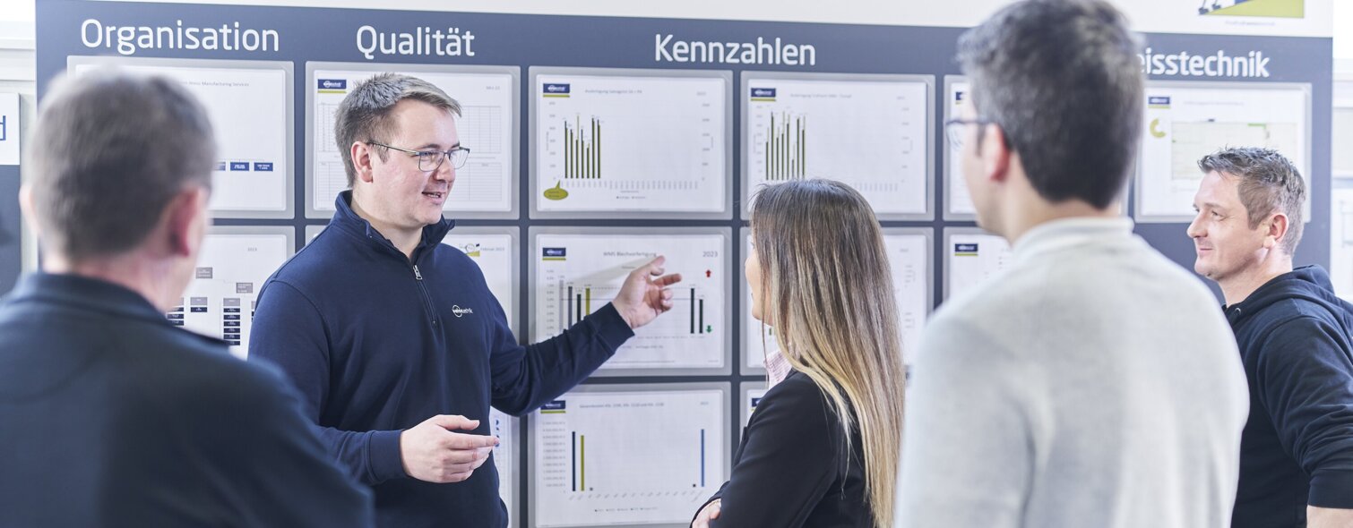 Mitarbeiter der Schunk Group bei einer Besprechung zu Kennzahlen vor einem Whiteboard mit verschiedenen Grafiken und Informationen