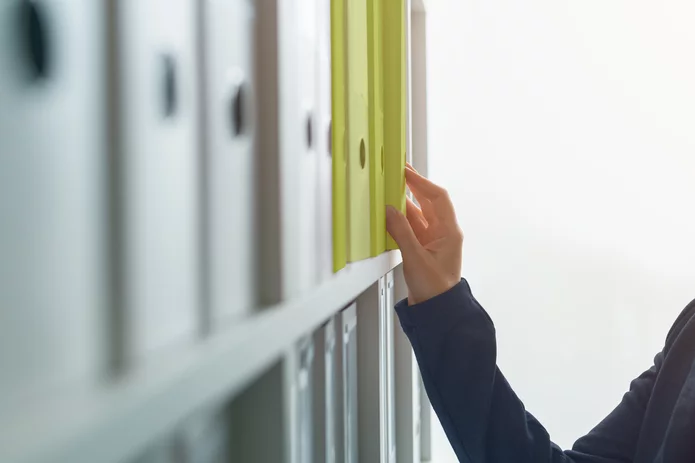  A person reaches into a shelf in the office with various folders and grabs a particular folder