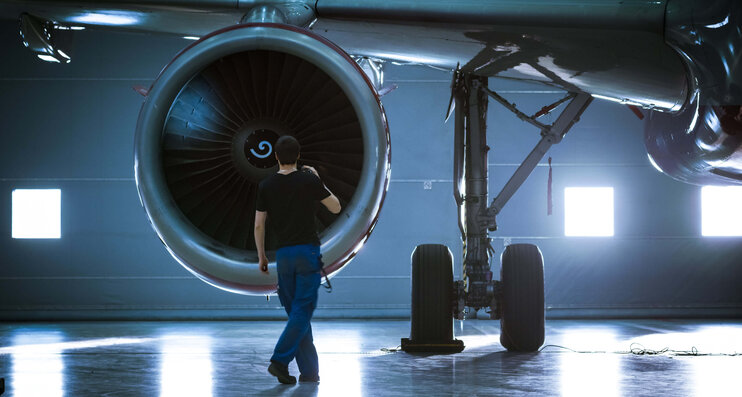 Flugzeugmechaniker arbeitet an der Turbine eines Flugzeugs und inspiziert diese mit einer Taschenlampe